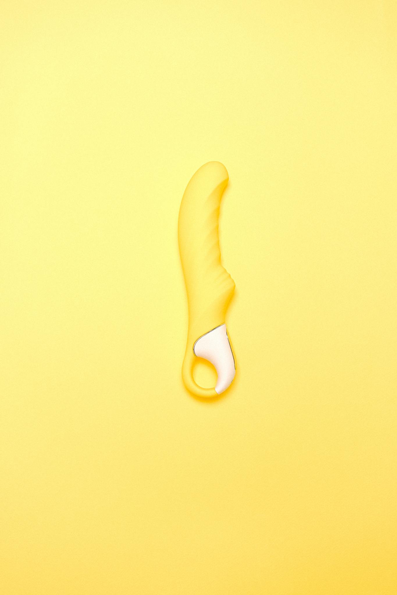 A yellow silicone vibrator displayed on a matching colored background, showcasing modern intimacy products.