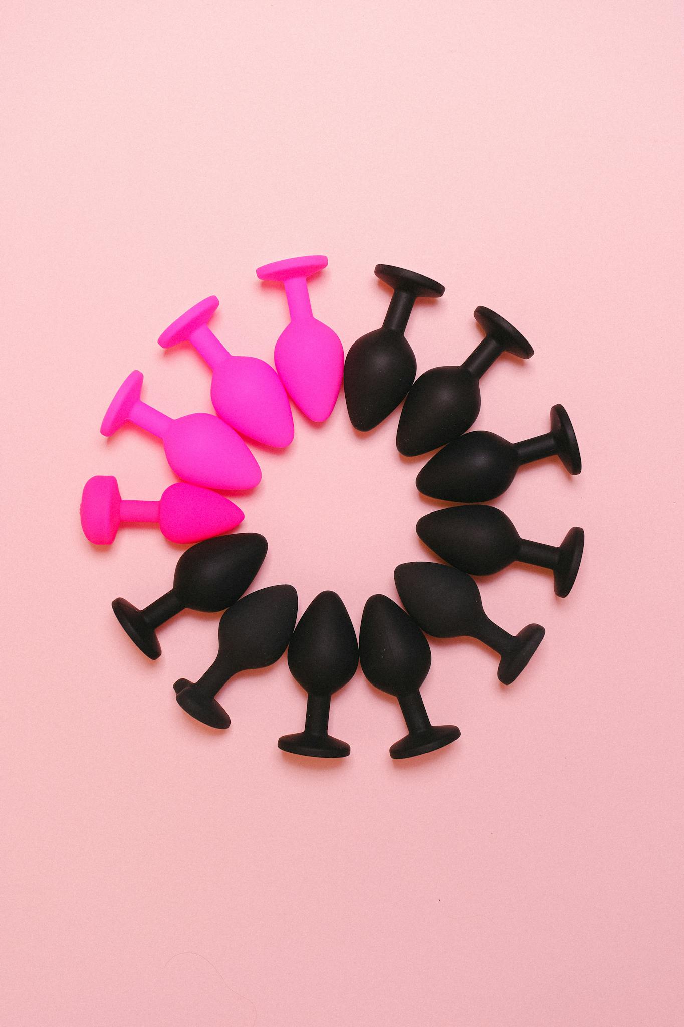 Colorful arrangement of silicone sex toys forming a circle on a pastel pink surface.